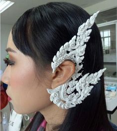 a woman with long black hair wearing a pair of white headpieces on her ear