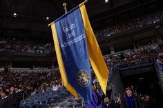 a person holding a blue and yellow flag in front of an audience at a graduation ceremony