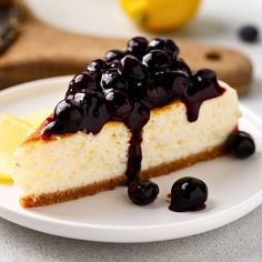 a slice of cheesecake with blueberries and lemon on a white plate next to some sliced lemons