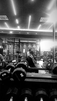 black and white photograph of people working out in a gym with lots of dumbbells