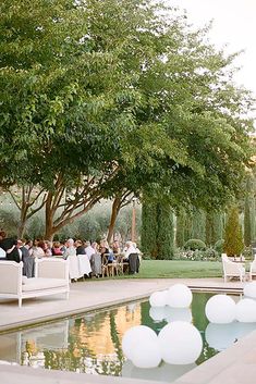 a group of people sitting at tables next to a pool with white balloons floating in the air