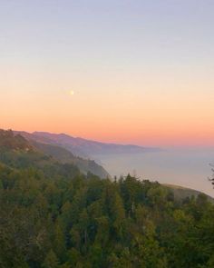 the sun is setting over some trees on top of a hill with mountains in the background