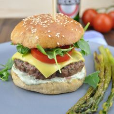 a hamburger with cheese, lettuce and tomato on a bun next to asparagus