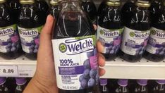 a person is holding up a bottle of weldich's grape juice in front of the shelves