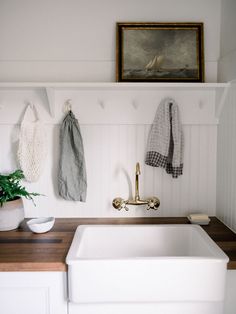 a white sink sitting under a painting next to a potted plant on top of a wooden counter