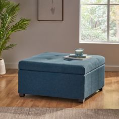 a blue ottoman sitting on top of a hard wood floor next to a potted plant