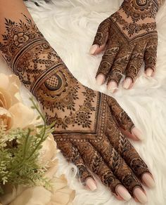 two hands with henna tattoos on them and flowers in the foreground, next to a white furnishing