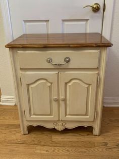 an old white cabinet with wood top and handles on the door handle, in front of a wall