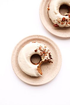 two donuts with white frosting and sprinkles are on small plates