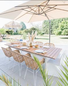 an outdoor dining table set with plates and bowls under an umbrella in the backyard area