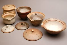 a group of ceramic bowls and lids on a gray table top, with one empty bowl in the middle