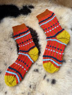 two pairs of colorful socks laying on top of a cowhide rug with black spots