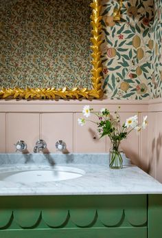 a bathroom sink sitting under a mirror next to a vase with flowers on top of it