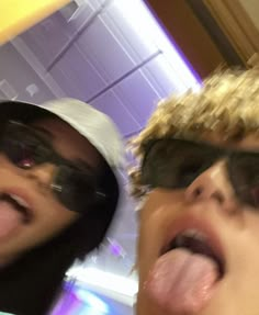 two people sticking their tongue out in front of the camera, one person with sunglasses on