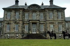 two horses are standing in front of an old building that is very large and has many windows