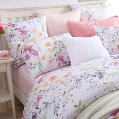 a white bed with pink and yellow flowers on the comforter, pillows and pillow cases