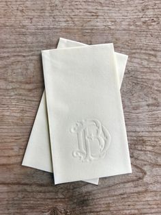 three white napkins with monogrammed initials on them sitting on a wooden table