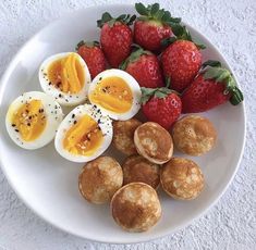 a plate with eggs, strawberries and muffins sitting on top of it