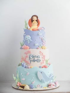 a three tiered cake decorated with an image of a mermaid and other sea creatures