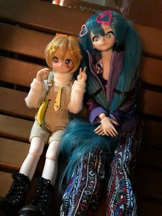 two dolls sitting next to each other on a bench