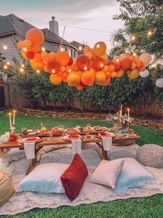 an outdoor dinner table with orange balloons hanging from the ceiling and pillows on the ground