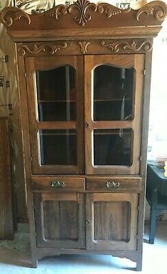 an old wooden china cabinet with glass doors and carvings on the front, sitting in a room