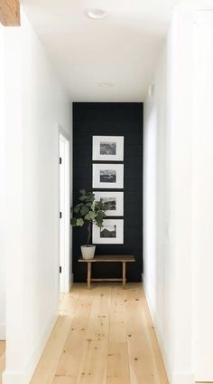 an empty hallway with black walls and white framed pictures on the wall, along with a wooden bench