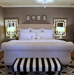 a white bed with black and white striped foot stool in front of the headboard