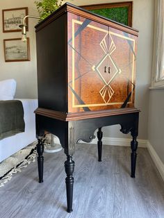 a black and brown cabinet sitting on top of a hard wood floor next to a bed