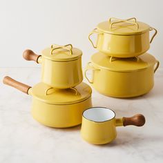 three yellow pots with wooden spoons on a white table