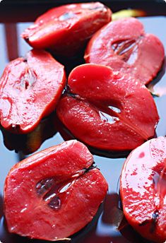 sliced red tomatoes sitting on top of a black tray with water droplets all over them