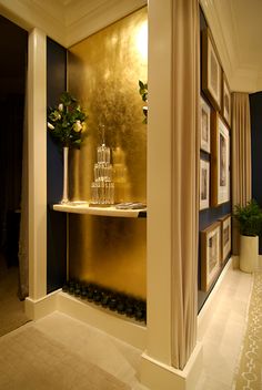 an elegant hallway with gold and blue walls, framed pictures on the wall and vases filled with flowers