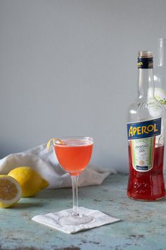 a bottle of aperoli next to a cocktail glass with a lemon slice on the side