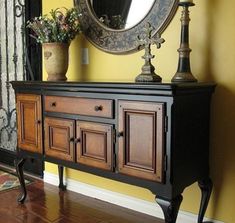 a black and brown dresser sitting next to a mirror on top of a wooden floor