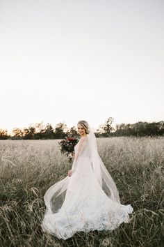 a woman in a wedding dress is walking through the grass with her veil over her face