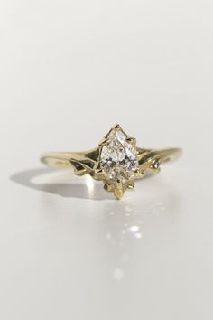 a yellow gold engagement ring with a pear shaped diamond in the center, on a white background