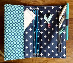 a blue and white dotted notebook with scissors, pen and paper clips on it sitting on a wooden table