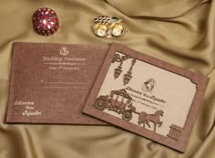 two wedding cards on a gold cloth next to an ornament and other items