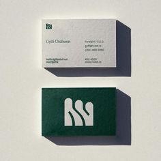 two business cards sitting side by side on top of a white surface with green lettering