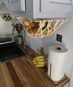 a kitchen counter with some fruit hanging from it's hooks and paper towel holder