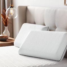 a close up of a bed with a pillow on top of it and a night stand in the background