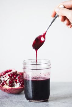 someone is pouring red liquid into a jar with pomegranate on the side