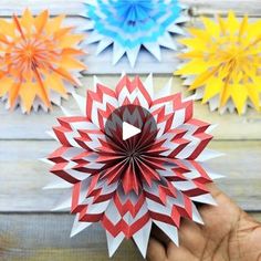 someone is holding an origami flower in front of four different colored paper flowers