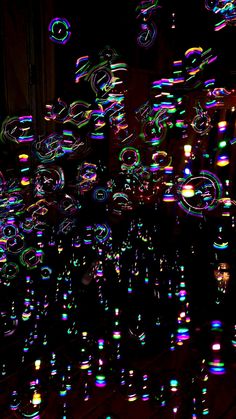 many bubbles are floating in the air at night with colored lights on them and dark background