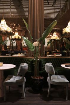 the interior of a restaurant with green velvet booths and white chairs, large plants in vases