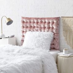 a white bed topped with a pink headboard next to a lamp and a brick wall