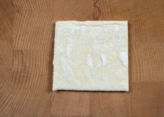 a square piece of white paper sitting on top of a wooden table next to a knife