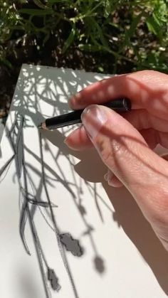 a person holding a pen and writing on a piece of paper with plants in the background