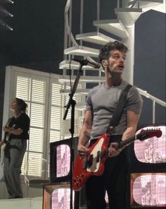 a man with a guitar standing in front of a microphone and some people on stage