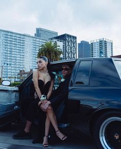 two women sitting in the back of a black car with their legs up on the door